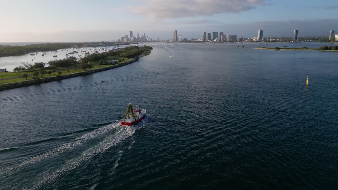 Aerial views over The Spit as a fishing trawler heads to the marina on the northern end of the Gold Coast in the morning on a sunny day.