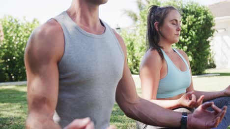 feliz pareja caucásica practicando meditación de yoga en un jardín soleado, cámara lenta