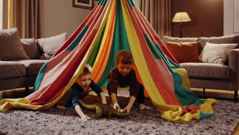 boys playing with dinosaur toys under a colorful blanket fort