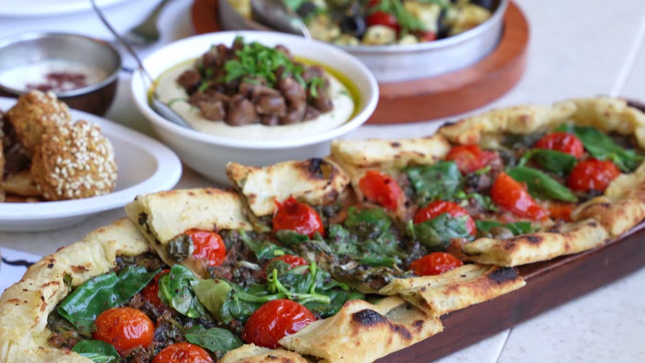 Close-up of a hand taking a slice of freshly baked flatbread pizza topped with cherry tomatoes, basil, and herbs — perfect for food, restaurant, and lifestyle marketing
