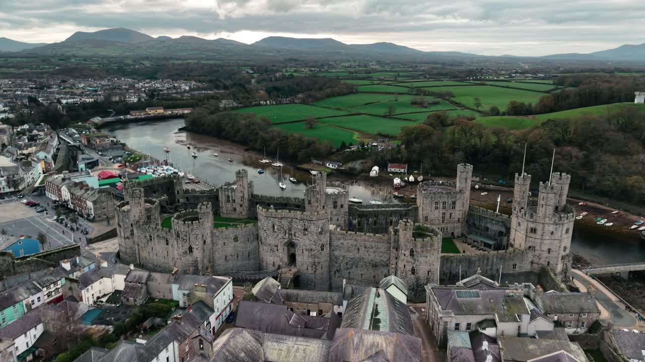 Majestic Caernarfon Castle drone clockwise rotate from far, beautiful estuary and mountains backdrop, North Wales, UK