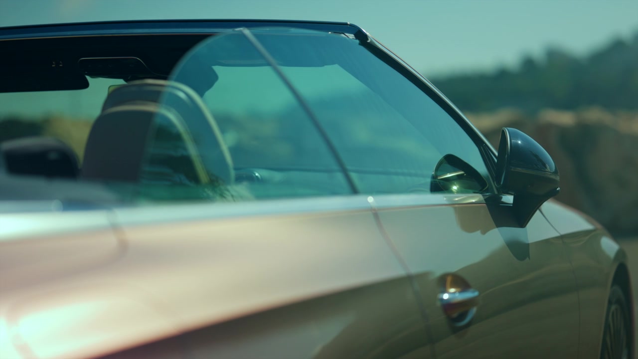 Sleek gold luxury convertible car from side view with window and rearview mirror, reflecting ambient light