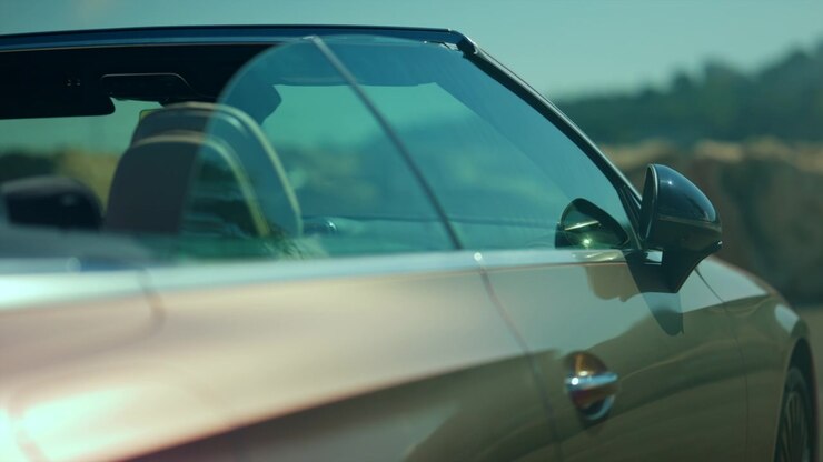 Elegante auto decappottabile di lusso color oro, vista laterale con finestrino e specchietto retrovisore, che riflette la luce ambientale.