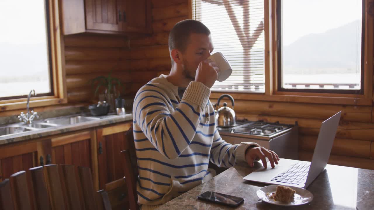 hombre caucásico pasando tiempo en casa, bebiendo una bebida, trabajando en una computadora portátil