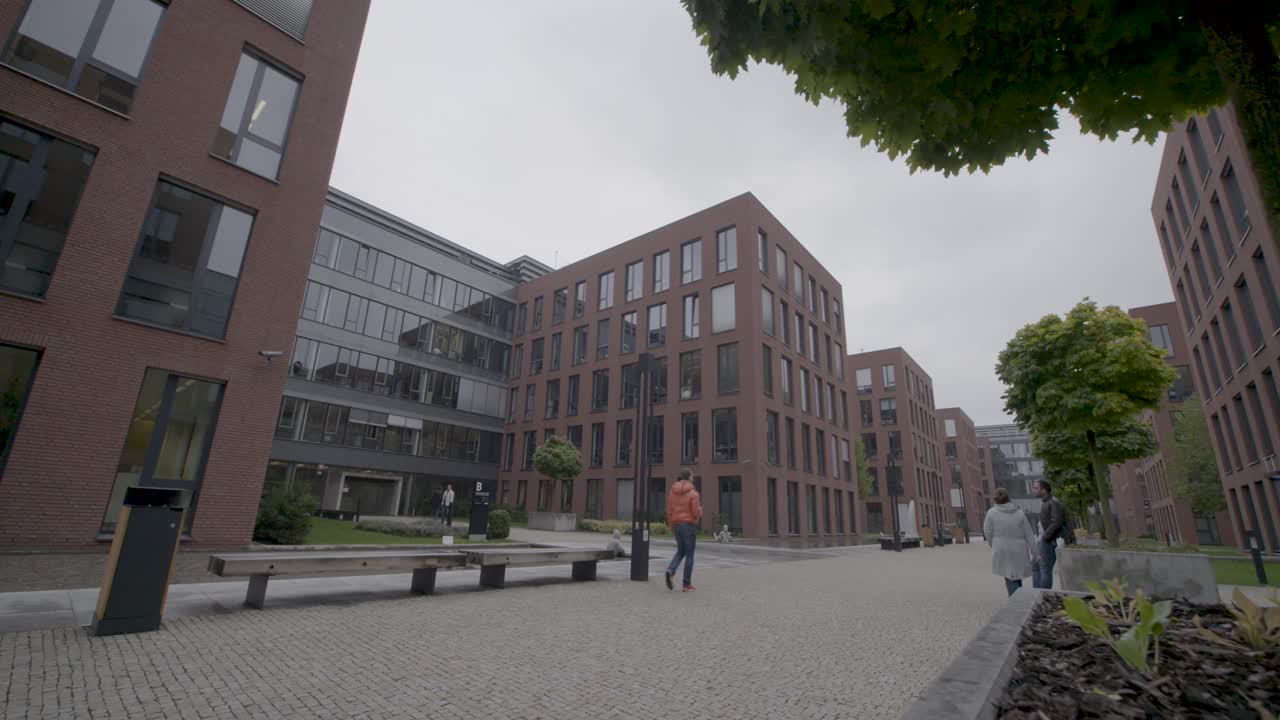 Modern urban courtyard with people walking on a cloudy day, panning shot