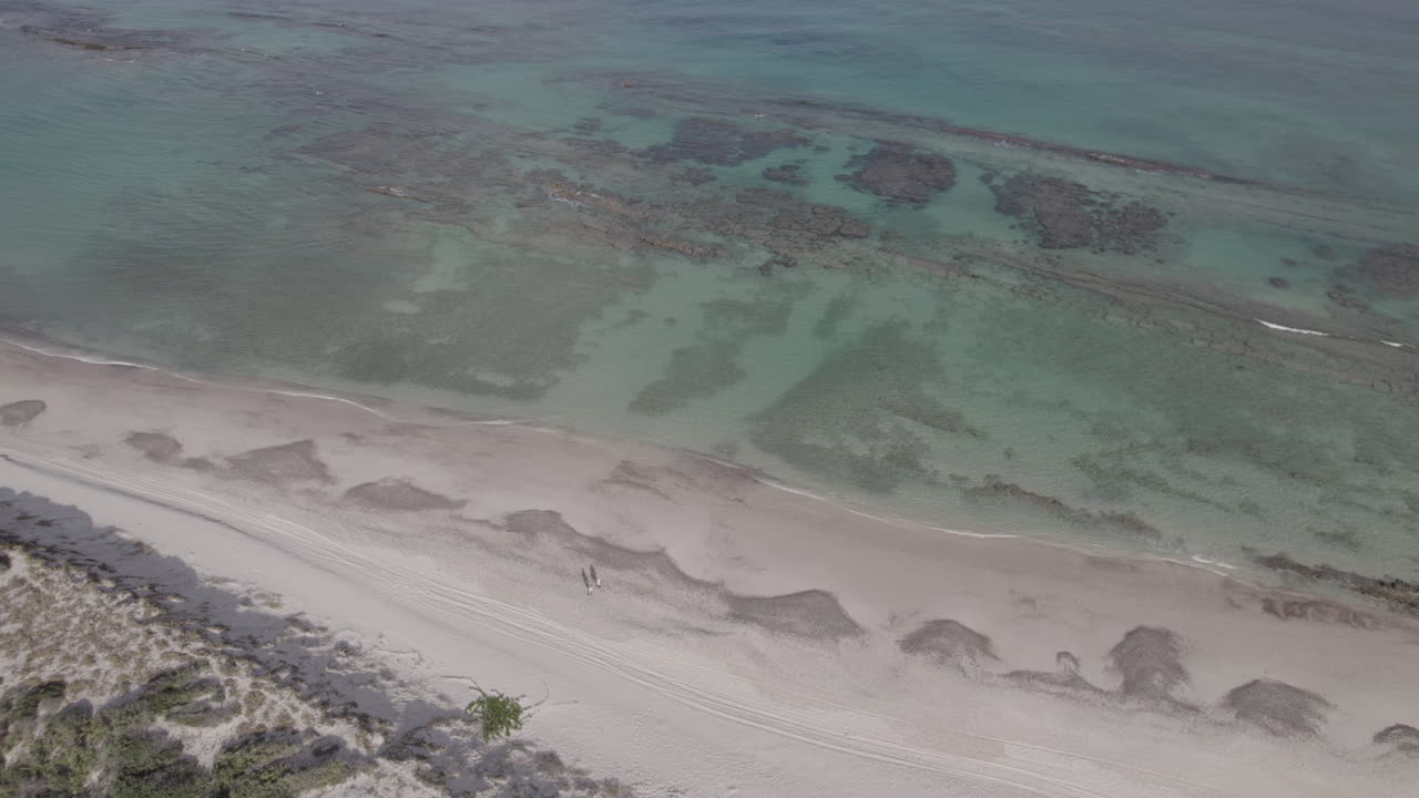 dos personas caminando juntas en una playa de arena durante la marea baja