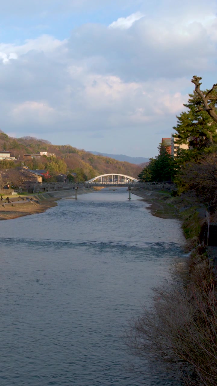 Inquadratura ampia statica di un fiume calmo che scorre attraverso una storica città giapponese sotto le nuvole