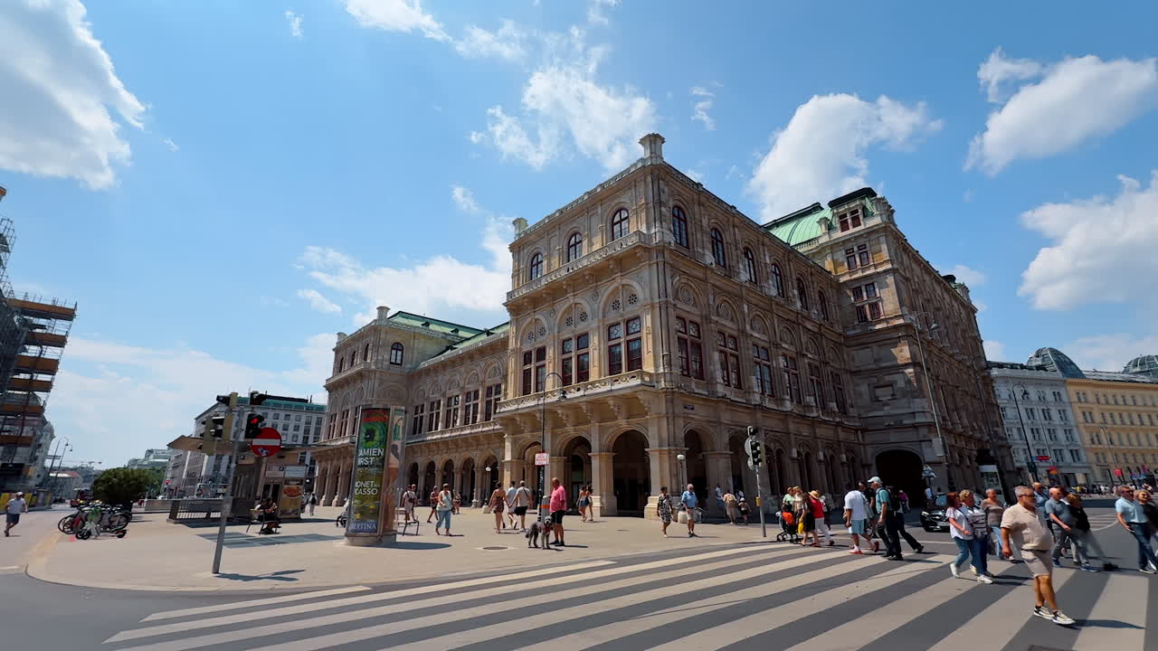 Vienna, Austria - June 9, 2025: Numerous people walk by the crossroads in Vienna, Austria. Low angle view at stunning buildings of the Vienna State Opera