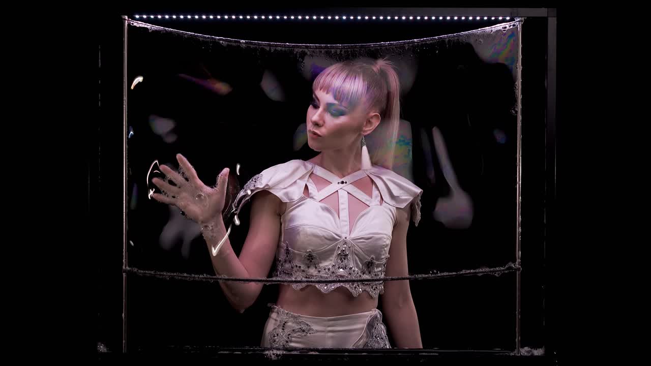 소녀는 비누 거품으로 트릭을합니다. 그녀는 빛을 반사하는 색 ⁇ 의 하이라이트로 비누 벽에 손으로 놀고 있습니다.