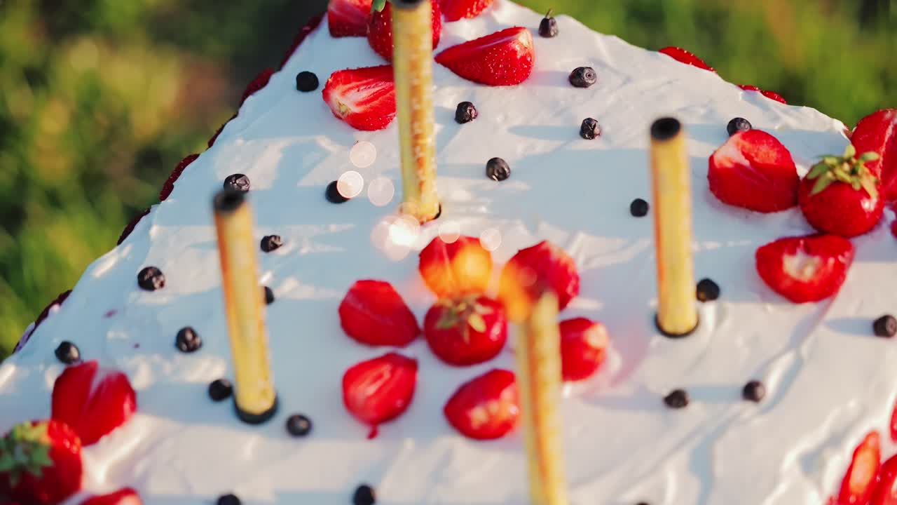 Slow motion, cake candles extinguish strawberries on white frosting at sunset