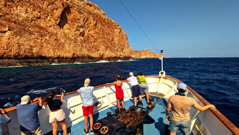 tourists on a boat admire rocky cliffs at kissamos port under clear skies and bright sunlight