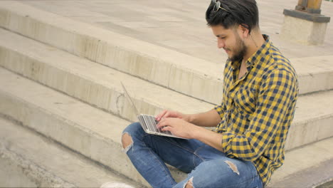 Gutaussehender-Mann,-Der-Auf-Treppen-Mit-Laptop-Im-Freien-Sitzt