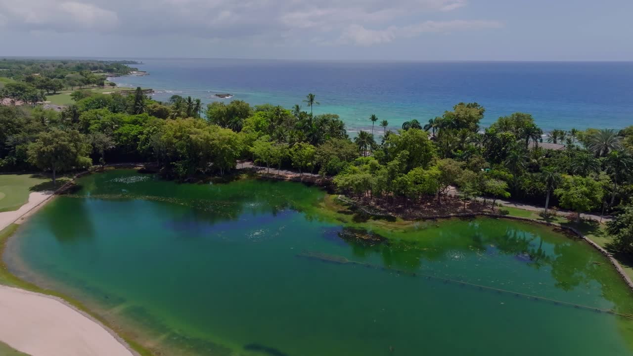 Sø og sandbunker på golfbane med havet i baggrunden i Casa de Campo, Den Dominikanske Republik. Fremadrettet luftfoto.