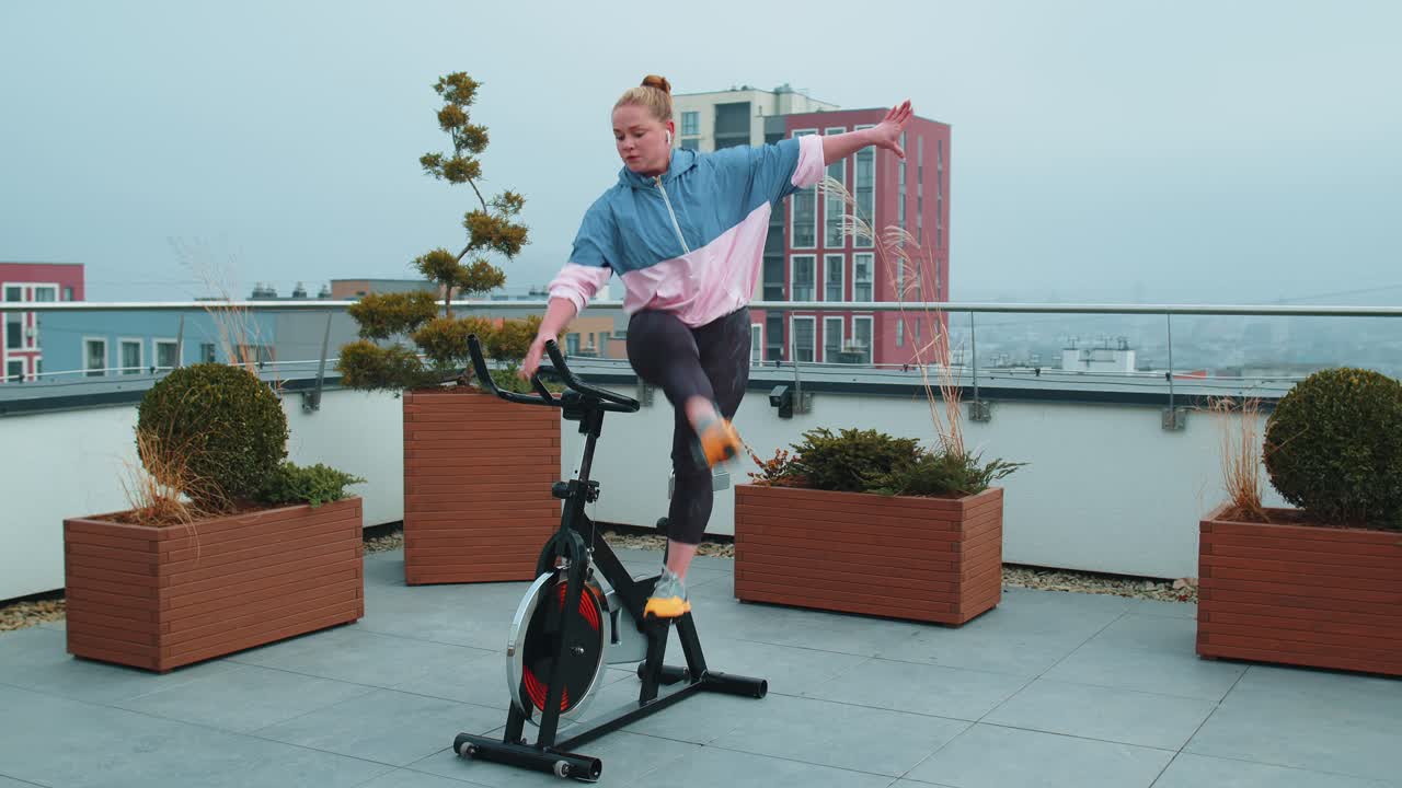 Athletic woman riding on spinning stationary bike training routine on house rooftop weight loss
