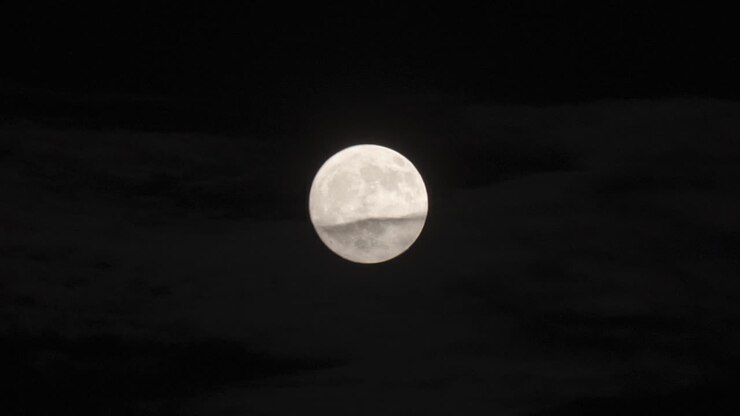 Grande lua cheia brilhando na escuridão devido ao efeito vibratório do calor.