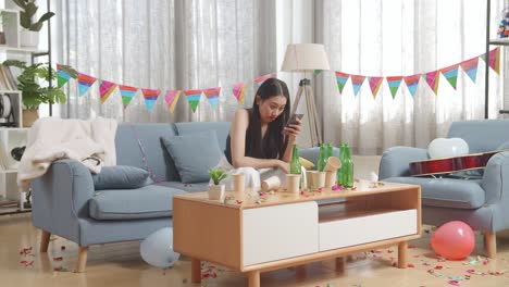 drunk asian woman sitting on a sofa and playing smartphone after having a party at home