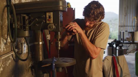 herrero caucásico con gafas de seguridad forjando herramientas metálicas en el taller