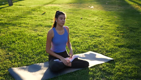 a fit young woman sitting in lotus position during meditation in the park at sunrise to improve her mental health