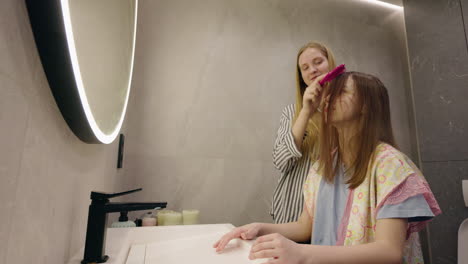 sister combing a girl's hair in the bathroom