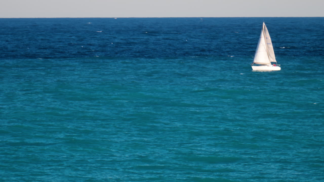 Distant view of a white sailboat floating on the blue sea