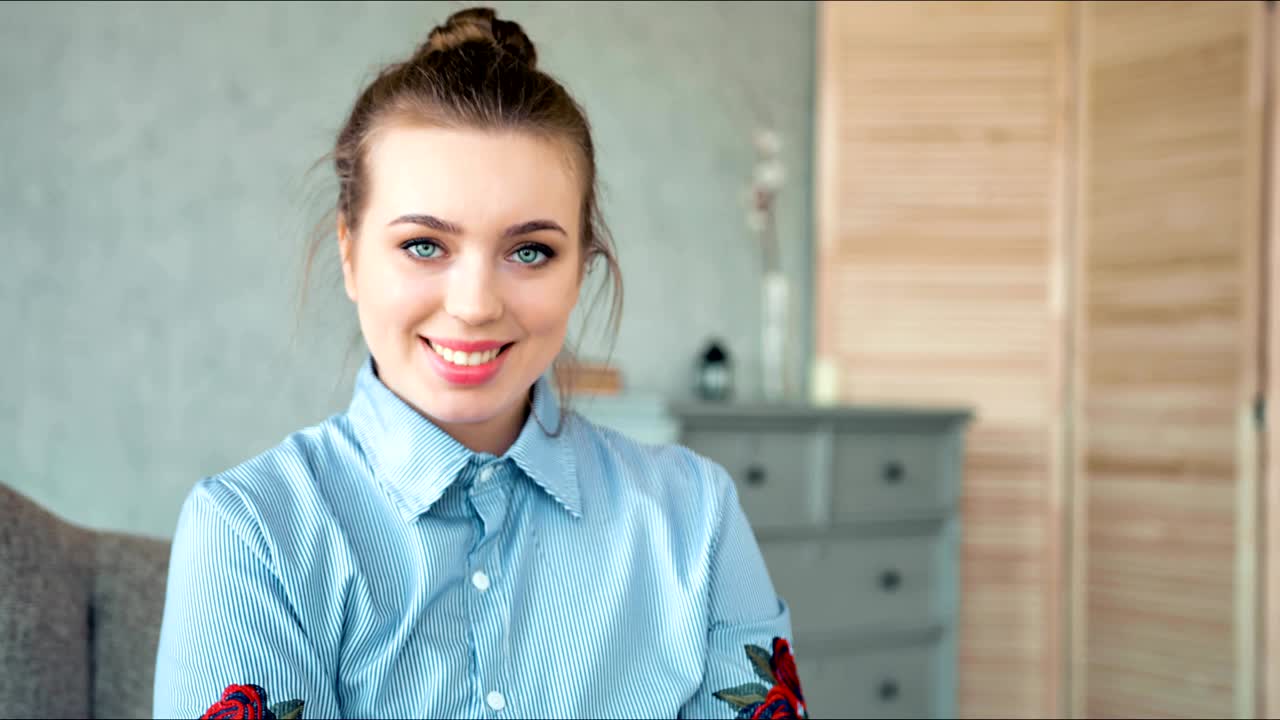 아름다운 미소를 가진 예쁜 여성이 집에서 카메라를 보고 있습니다.