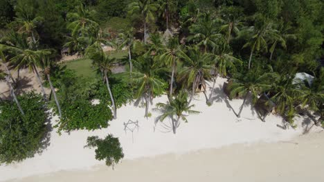 Traditionelle-Hütten-Und-Palmenhängematten-Am-Tropischen-Kokosstrand-Mit-Menschen,-Die-Auf-Einer-Baumschaukel-Reiten