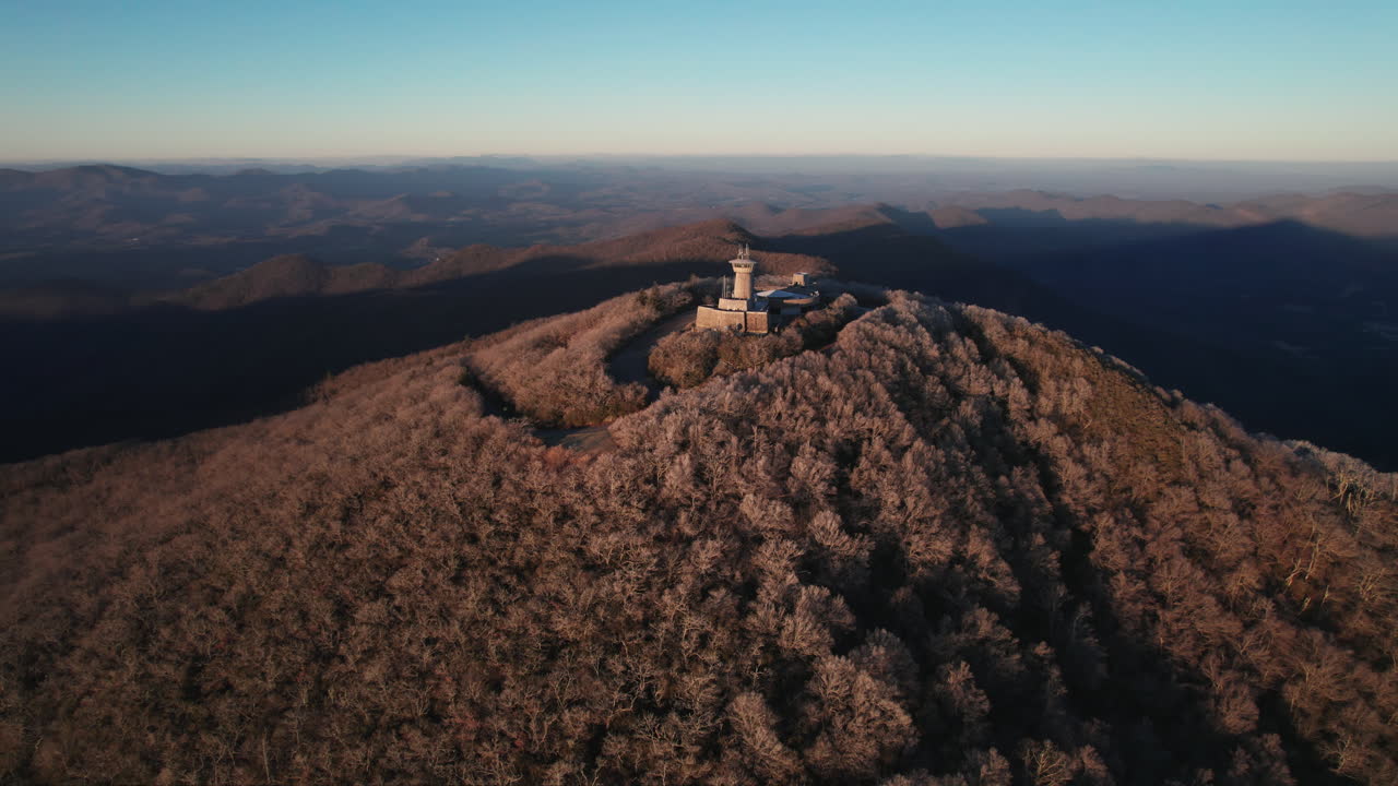 A cinematic aerial of the Brasstown Bald summit lookout, a popular state park with warm morning light casting rays and shadows over the rolling hills of the Blue Ridge mountain range in Georgia,