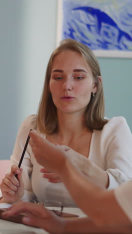 brunette woman with disability hands red pencil to blonde friend sitting at table. female students work on joint educational project together closeup