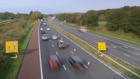 Busy-motorway-with-lane-closure-and-slowed-traffic-with-trains-traveling-in-both-directions-on-left-of-frame