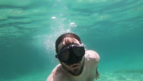 Front-view-of-a-man-diving-and-blowing-bubbles-from-his-mouth-in-slow-motion-in-a-turquoise-sea