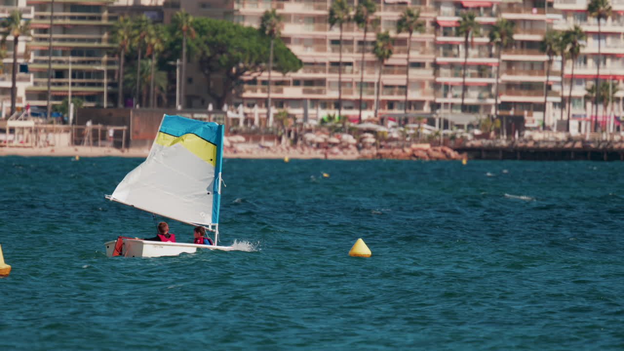 Children in small sailboats learning to navigate on the blue sea near a beach resort
