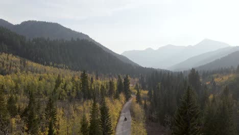 Drone-rising-up-over-Utah-forest-and-ATV,-mountains-in-background