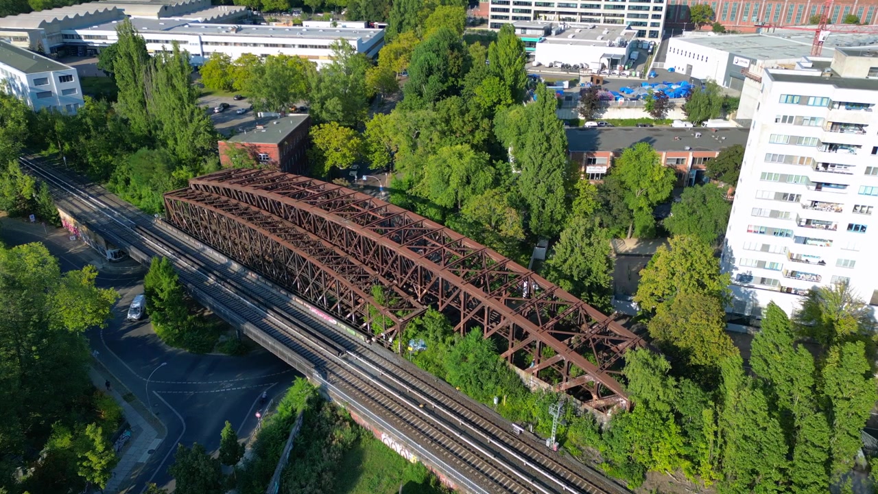 Rusten jernbanebro over togskinner i frodigt grønt bymiljø i Berlin, Tyskland, transportinfrastruktur. Jævn luftfoto droneflyvning oppefra.