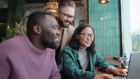 diverse colleagues working on laptop and speaking in cafe