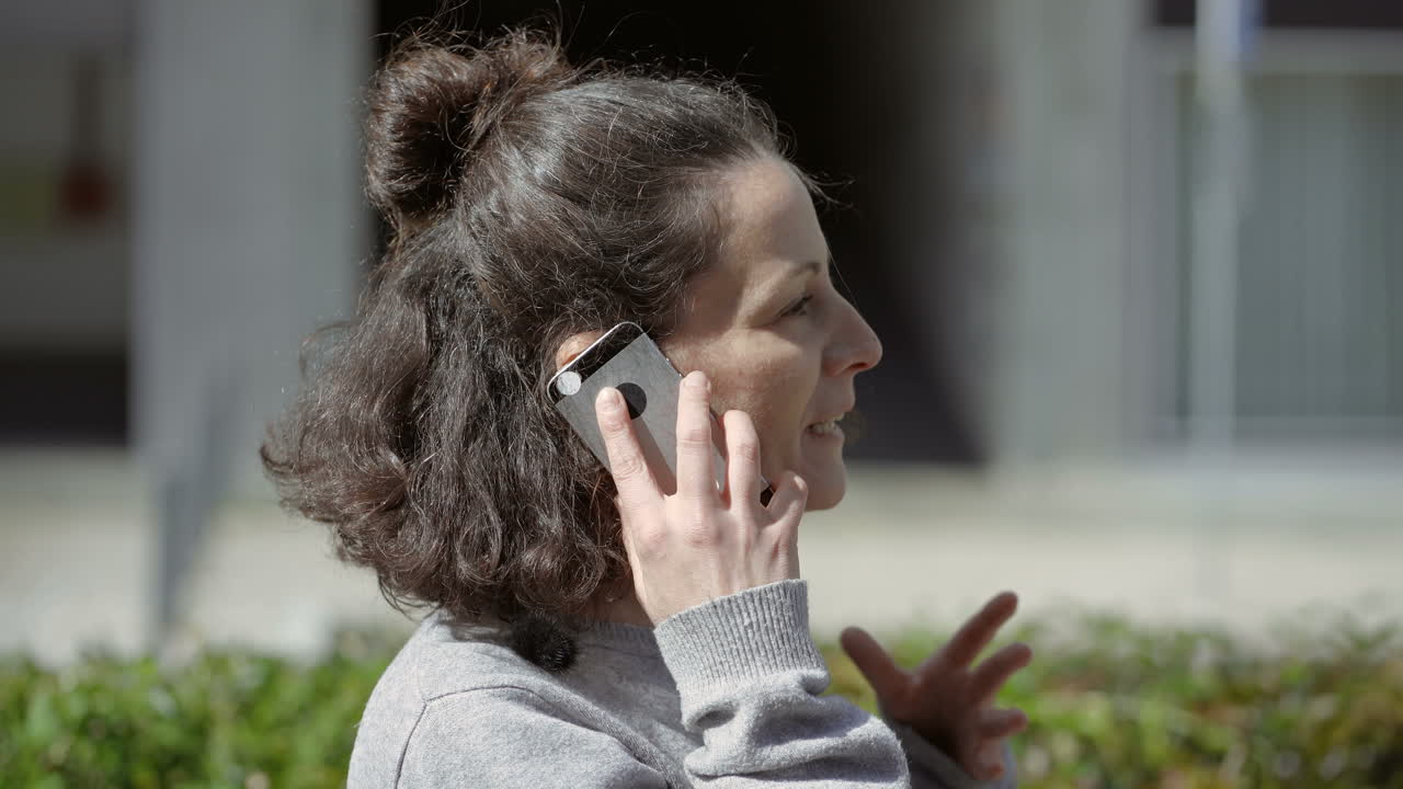 mujer morena feliz hablando en el teléfono inteligente al aire libre.