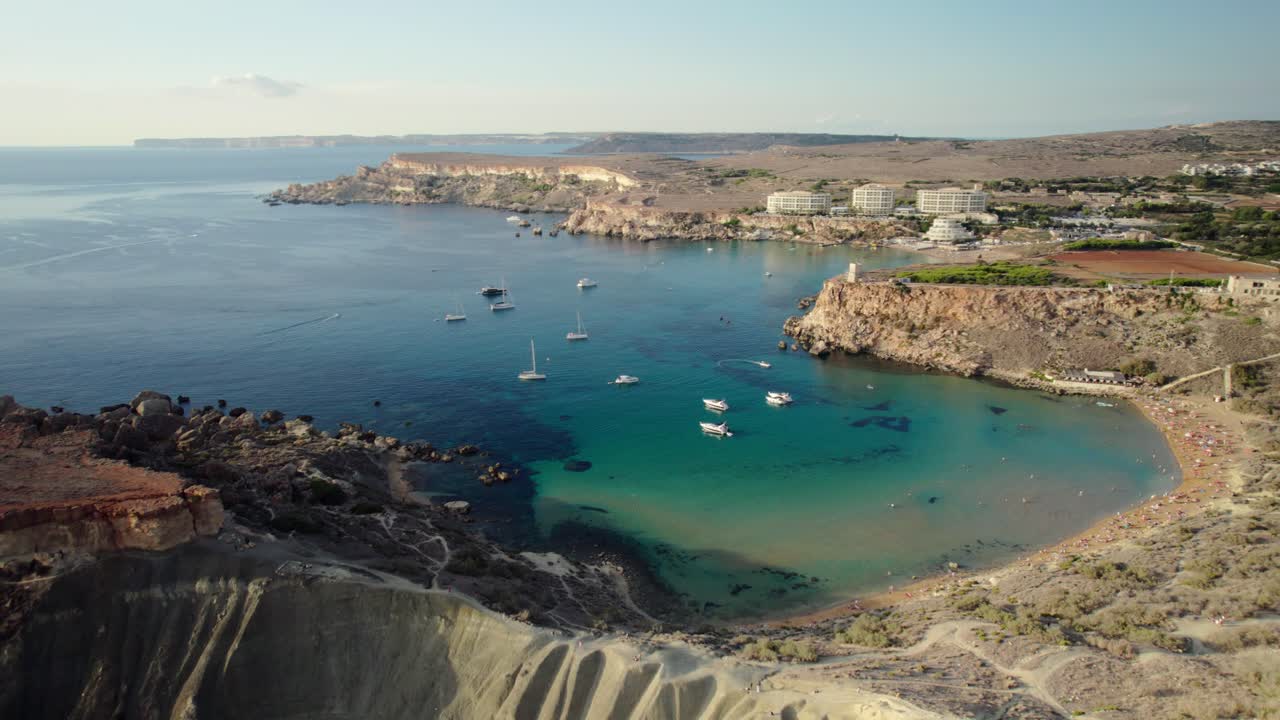 Movimento aereo diagonale che mostra scogliere, barche e costa nella Golden Bay di Malta