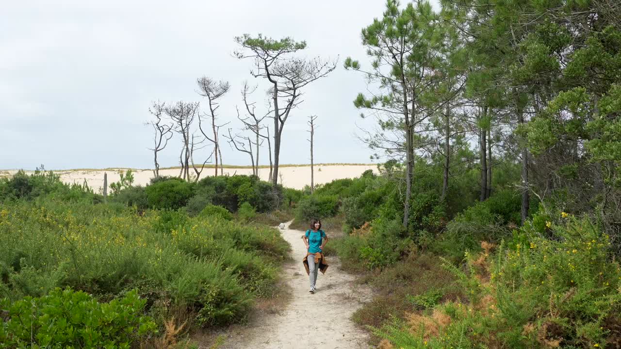 Mulher Caminhando em Caminho Arenoso por Floresta Verde Rumo a uma Duna de Areia