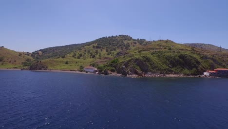 Antenne:-Eine-Griechische-Flagge-Auf-Einem-Felsen-Weht-Im-Wind-Auf-Der-Insel-Lesbos,-Griechenland