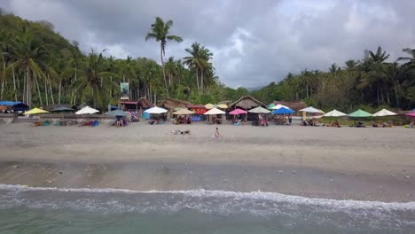 Perfect-aerial-view-flight-slider-fly-sideways-from-right-to-left-drone-shot-of-a-instagram-spot-on-a-dream-Beach-with-parasol,-Palm-Trees-and-nice-waves-at-Nusa-Penida