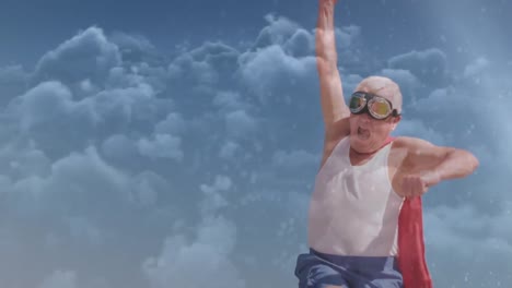 Animation-of-clouds-over-happy-senior-caucasian-man-wearing-superhero-costume-on-beach