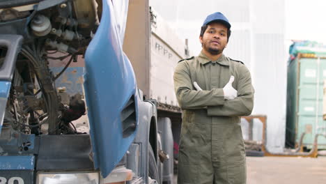 worker fixing a truck in a logistics park, then looks at the camera with crossed arms