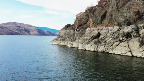 slide shot across kamloops lake towards rocky bedrock cliffs on a sunny day in autumn