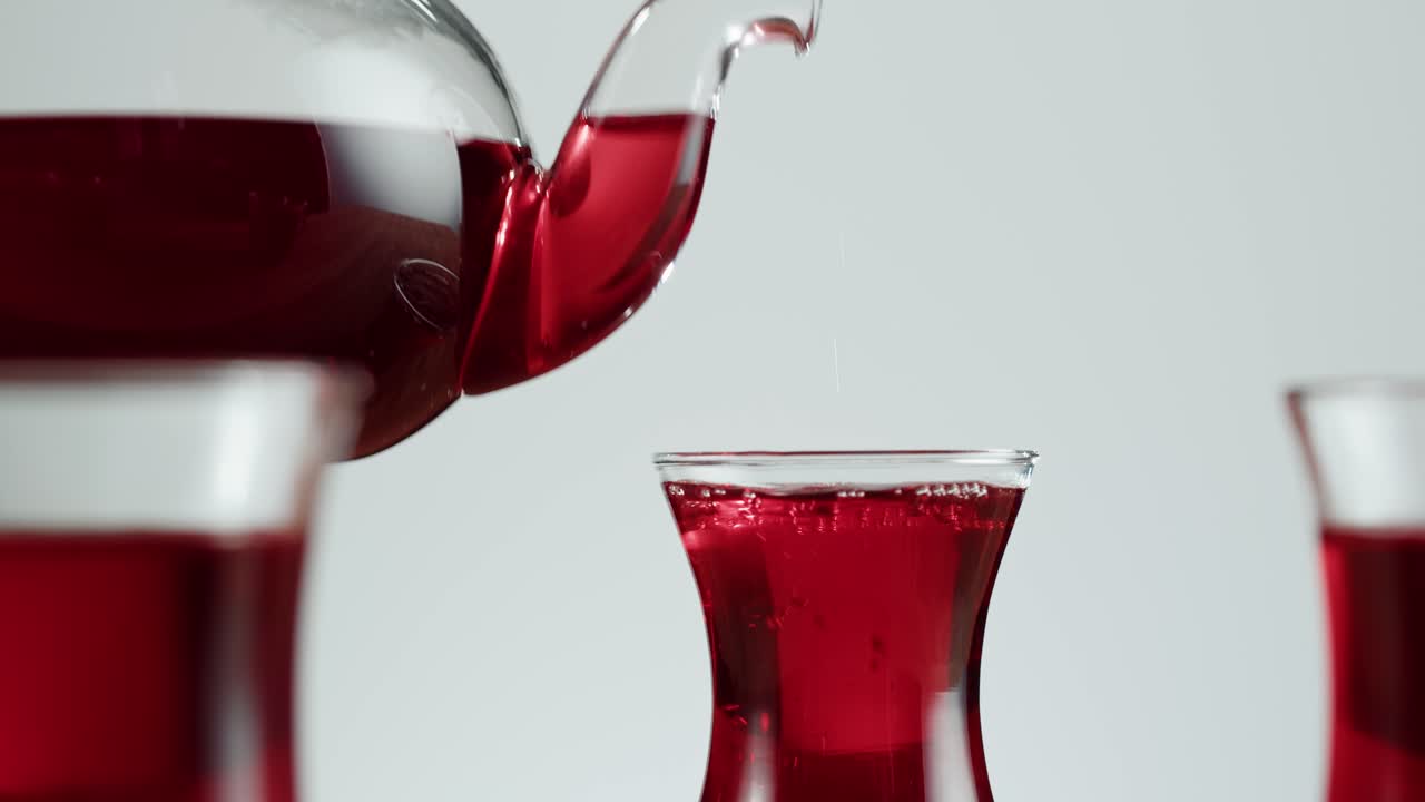 Red Liquid Being Poured from a Glass Teapot into a Glass Cup