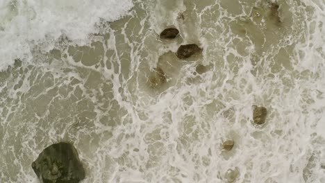 aerial top view in slow motion of the sea tide flooding into the rocks