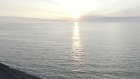 drone shot, flying backwards, past a carved out rock formation, away from a sunset over a lake