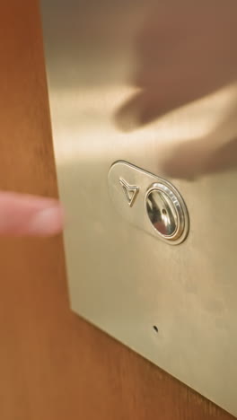 first-person view captured with a handheld camera showing a person's finger pressing the elevator button. the close-up shot highlights the moment of interaction with the elevator panel