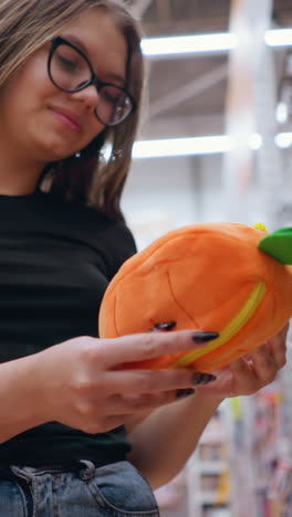primer plano de una mujer con gafas seleccionando un bolso naranja y verde brillante de un estante de la tienda, la compradora navega por accesorios elegantes en un entorno minorista