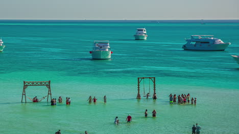 turistas de lapso de tiempo esperando los columpios de la playa en el agua turquesa mientras los barcos navegan