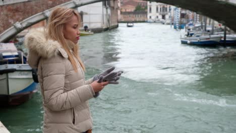 Philippina-Steht-An-Einem-Kanal-In-Venedig-Und-Zieht-Handschuhe-An,-Um-Sich-Vor-Der-Kälte-Zu-Schützen,-Während-Sie-Die-Vorbeifahrenden-Kanalboote-Beobachtet