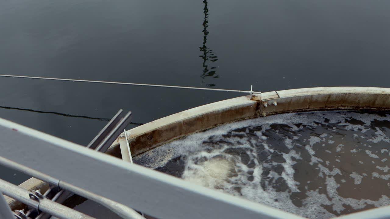 A wastewater treatment clarifying pond reflects the surrounding structure as water flows in, capturing the serene yet industrial motion of the purification process